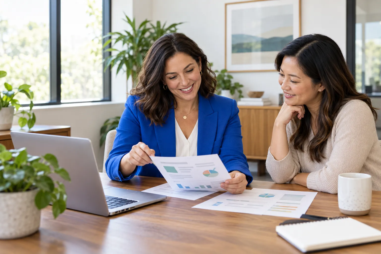 Two benefits leaders at a conference table going over printed plan cost reports beside a laptop.